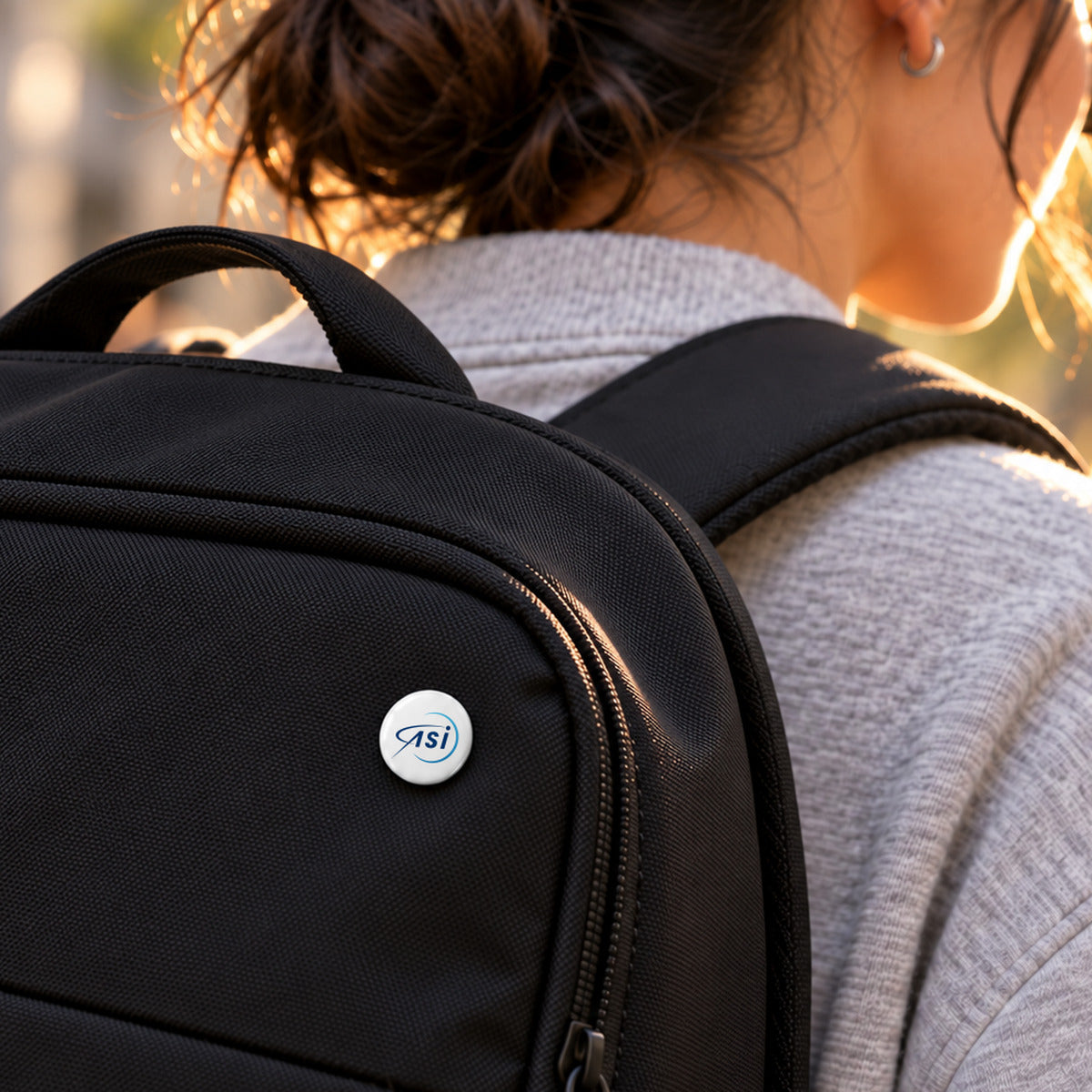 ASI 25 mm pin on a black backpack, worn on a city street